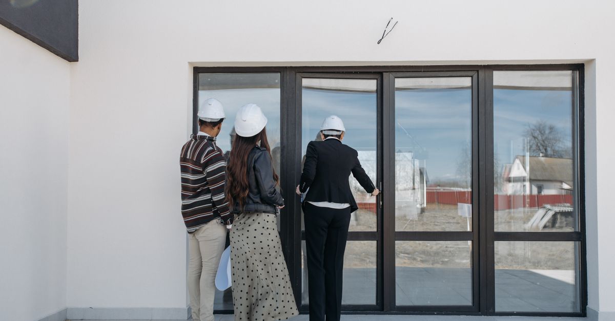 Real estate agents in helmets showing a new house to clients through glass doors.